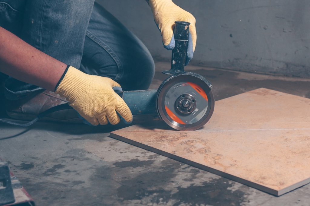 worker in gloves cutting tile with angle grinder